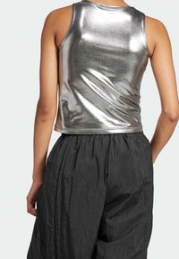 Top sin mangas de color plateado metálico con un diseño ajustado, que presenta una textura suave y brillante y un corte corto, combinado con pantalones negros sueltos.