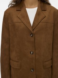 Abrigo marrón de gamuza con botones y cuello solapa, llevado sobre una camiseta blanca de canalé con cuello redondo, mostrado desde los hombros hasta la mitad del torso.