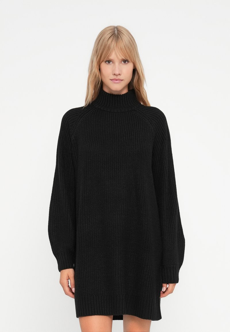 Melna adīta kleita ar augstu apkakli, garām piedurknēm un ribotu aproci. Iespējo brīvu piegriezumu un strukturētu rakstu. Gluda auduma.