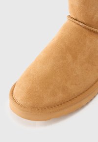 Bottine en suede beige à bout rond, surface texturée et semelle en caoutchouc. Présente une couture le long du bord.