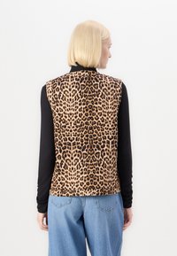 Γιλέκο από λεοπάρ σε μαλακό ύφασμα, με εφαρμοστή σχεδίαση, στρογγυλή λαιμόκοψη και χωρίς μανίκια, συνδυασμένο με ανοιχτό μπλε τζίν.