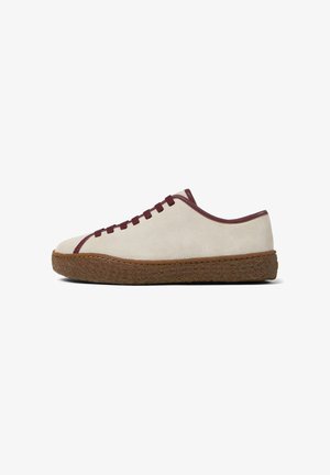 Zapatilla de ante beige con detalles burdeos, diseño con cordones, puntera redondeada y suela de goma marrón texturizada. Silueta minimalista y de perfil bajo.
