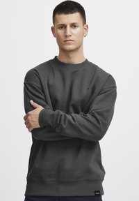 Dark gray fleece sweatshirt with a crew neckline, ribbed cuffs, and hem. Features a subtle logo on the front and label on the side.