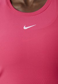 Top deportivo rosa de algodón suave con cuello redondo y ribetes acanalados. Presenta un logo de swoosh blanco de Nike en el pecho.
