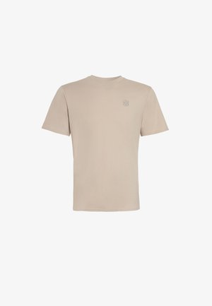 Camiseta beige de manga corta y cuello redondo con un pequeño logo bordado en el pecho izquierdo, mostrada sobre un fondo blanco liso.