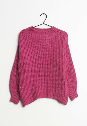 Pull en grosse maille rose avec poignets et ourlet côtelés suspendu à un cintre noir sur fond blanc.