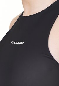 Crni bezrukavni odjevni predmet od glatkog materijala, s visokim ovratnikom i brendom "PEGADOR" u srebrnom tekstu na lijevoj strani prsnog područja.