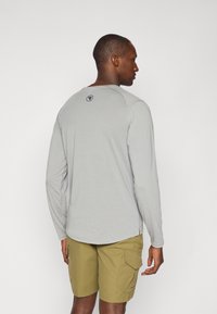 Long-sleeve gray shirt in lightweight fabric with a round neck. Notable logo on the back. Paired with olive green cargo shorts.