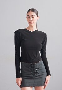 Top negru cu mâneci lungi și decolteu în V, având umeri structurați, asociat cu o fustă mini gri cu detalii cu șireturi în față.