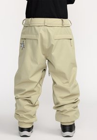Beige cargobroek met een relaxte pasvorm, voorzien van meerdere met rits gesloten zakken, elastische boorden en een geborduurde sterdetails op de achterkant.