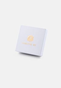 Valkoinen tekstuurilla varustettu lahjalaatikko, jossa on kultapainettu logo ja teksti "GINETTE NY" edessä, esittää minimalistista muotoilua.