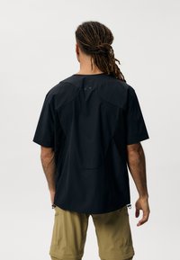 Kratka majica s kratkimi rokavi črne barve z mrežastim hrbtom, ki ima nastavljiv rob in okrogel izrez. Narejena iz lahkotnega materiala.