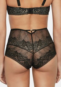 Zwarte, hooggesneden slip met kant, voorzien van een bloemenpatroon, doorschijnende stof en een gouden accent aan de achterkant, met een getand randje langs de randen.