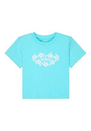 Meisje met lang haar dat een lichtblauw cropped t-shirt met bloemenprint draagt en donkerblauwe denimshorts, poserend met één hand op de heup.