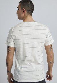 Balta trumpomis rankovėmis t-shirt marškiniai su mėlynomis horizontaliomis juostelėmis, apvalia iškirpte ir laisvu siluetu. Pagaminta iš medvilnės, turinti lygią tekstūrą.