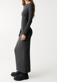 Langes, figurbetontes, dunkelgraues Kleid mit langen Ärmeln, aus strukturiertem Stoff. Kombiniert mit klobigen schwarzen Plateaustiefeln.