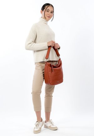 Borsa in pelle marrone dalla forma morbida con chiusura a zip, abbinata a un dolcevita a coste crema e pantaloni beige aderenti, indossati in modo casual.