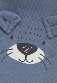 Blauem Stoff mit einem bedruckten Tiergesichtdesign in Schwarz-Weiß-Akzenten; beinhaltet strukturierte Kanten, die Ohren und Schnurrhaare ähneln.