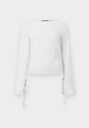 Biała dopasowana bluzka z długim rękawem, wykonana z teksturowanej tkaniny, z wiązaniami przy nadgarstkach, z prostym dekoltem i krótkim krojem.