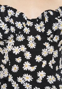 Svart tyg med vita prästkragar och gula mittar på en smockad bystdel av plagget.