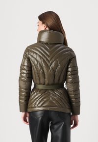 Olive green puffer jacket with chevron quilted pattern, high collar, and belted waist. Made of shiny, textured fabric with long sleeves.