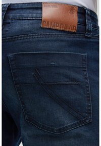 Dunkelblaue Jeans aus Denim mit einem braunen Leder-Label der Marke, ausgestattet mit einer Gesäßtasche mit einzigartiger Nahtdetail. Glatte Textur, lässiges Design.