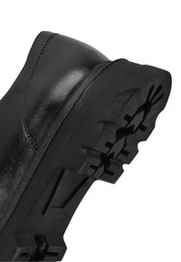 Semelle de chaussure en cuir noir avec des crampons profonds et robustes et une couture détaillée le long du bord supérieur, inclinée pour la traction et la durabilité.