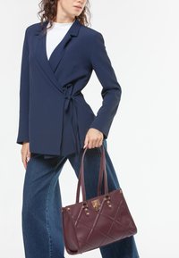 Blazer navy con cinturón a la cintura, combinado con pantalones de mezclilla de pierna ancha. Sosteniendo un bolso burdeos, con patrón acolchado y herrajes dorados.