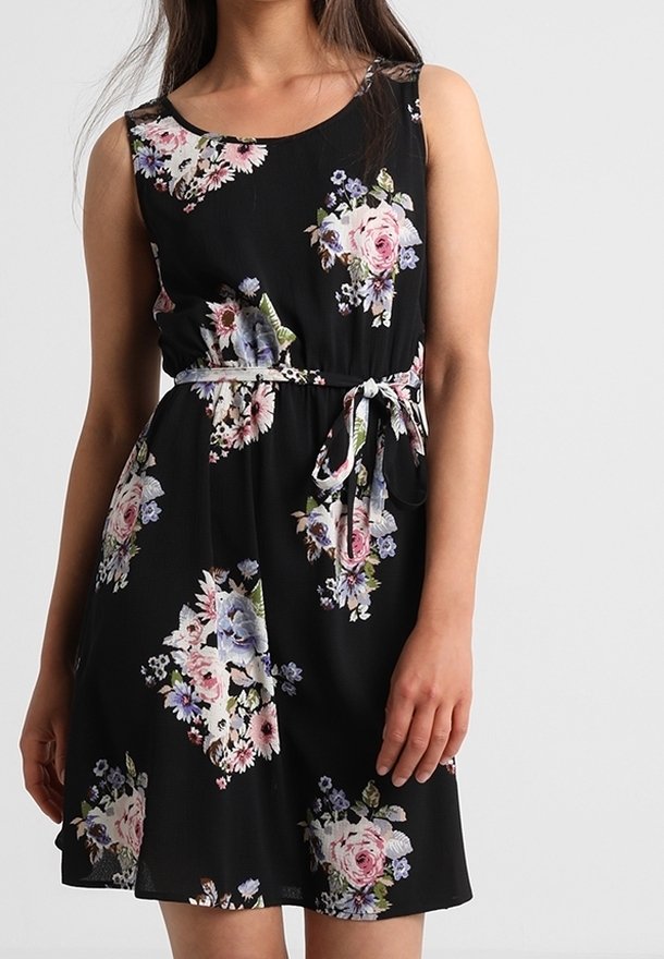 Květinové černé šaty s přiléhavým tělem, bez rukávů a se staženým pasem. Materiál vypadá lehce a má hladkou texturu.