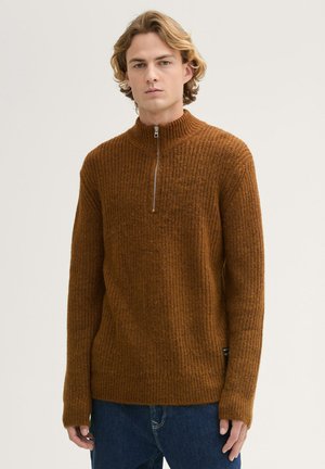 Brauner Strickpullover mit hohem Kragen und halbem Reißverschluss. Verfügt über ein strukturiertes Muster und eine lockere Passform, hergestellt aus einem weichen Material.