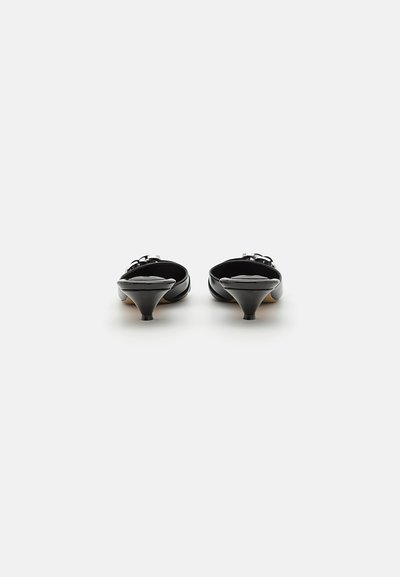 Mules de piel negra con tacón, con puntera puntiaguda, un pequeño tacón cónico y herrajes decorativos en la correa. Textura suave y diseño elegante.