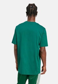 Zelené bavlněné tričko s krátkým rukávem a kulatým výstřihem, s volným střihem a hladkou texturou, kombinované s odpovídajícími zelenými kalhotami.