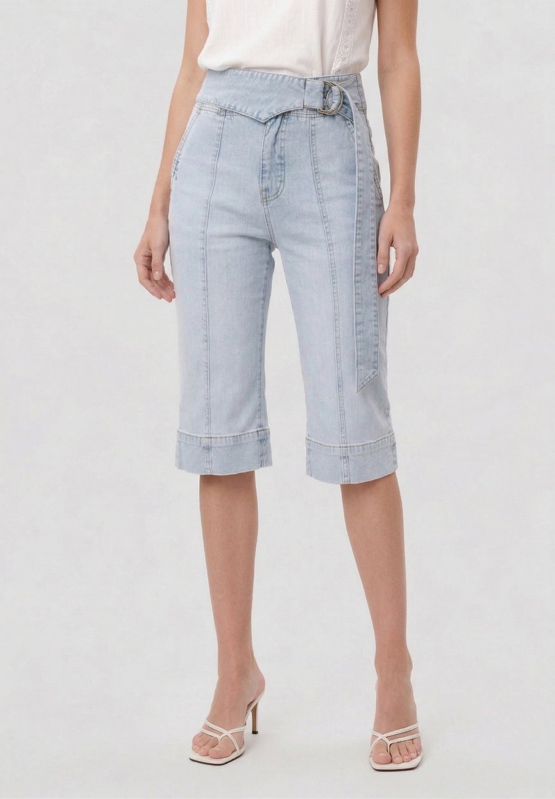 Ανοιχτό μπλε σορτς μπέρμουδα από τζιν με ψηλή μέση, γυρισμένα μπατζάκια και ταιριαστή ζώνη, φορεμένα με λευκές πέδιλα με λουράκια και αμάνικο πουκάμισο.