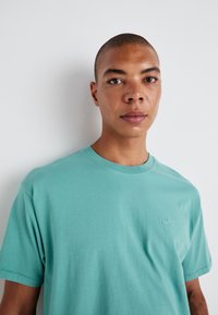 Tyrkis bomull t-skjorte med rund hals og korte ermer, med en liten brodert Levi's-logo på brystet. Glatt tekstur.