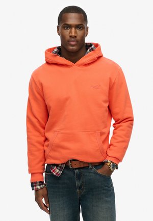 Orange huva sweatshirt med en framficka, med en rutig skjorta som syns under och blå denimjeans.
