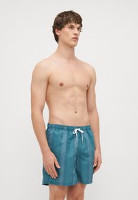 Tyrkysové plavky krátkeho strihu s elastickým pásom a bielou šnúrkou. Hladká textúra s jemným leskom, dĺžka po kolená, bez viditeľných vzorov.