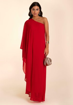 Vestido de noche rojo, de un solo hombro, hecho de una tela fluida, con un dobladillo asimétrico y un sobreposición drapeada. Acompañado de un pequeño bolso plateado.