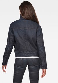 Mörk denimjacka med en figurnära design, hög krage och synliga sömnadsdetaljer. Slen yta, lätt tyg och kort längd.