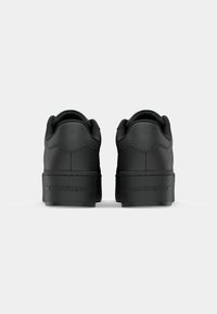 Black sneakers with a smooth leather-like material, rounded toe, low-top design, and embossed "TOMMY JEANS" logo on the heel.