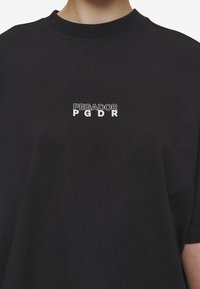 Zwarte katoenen t-shirt met een witte bedrukte logo met de tekst "PEGADOR PGDR" in een eenvoudige, vetgedrukte lettertype op de voorkant. Korte mouwen, ronde hals.