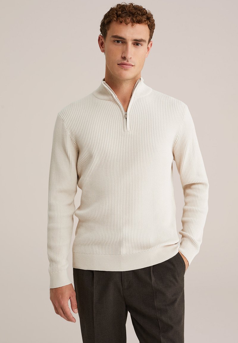Pulover bej deschis cu guler zip, textura rib a, mâneci lungi și un design ajustat. Asortat cu pantaloni negri.