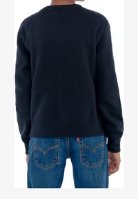 Felpa blu navy con scollatura e polsini a coste, abbinata a jeans blu con cuciture classiche delle tasche posteriori e dettagli del logo.