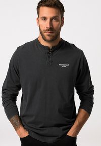 Langärmliges schwarzes Shirt aus Baumwolle mit einem geknöpften Henley-Ausschnitt und einem kleinen weißen Logo auf der Brust, mit lockerem Schnitt.