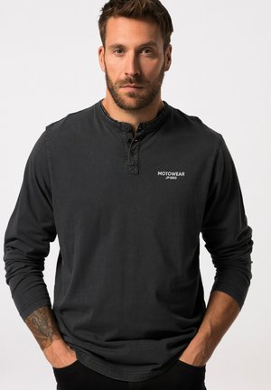 Langärmliges schwarzes Shirt aus Baumwolle mit einem geknöpften Henley-Ausschnitt und einem kleinen weißen Logo auf der Brust, mit lockerem Schnitt.