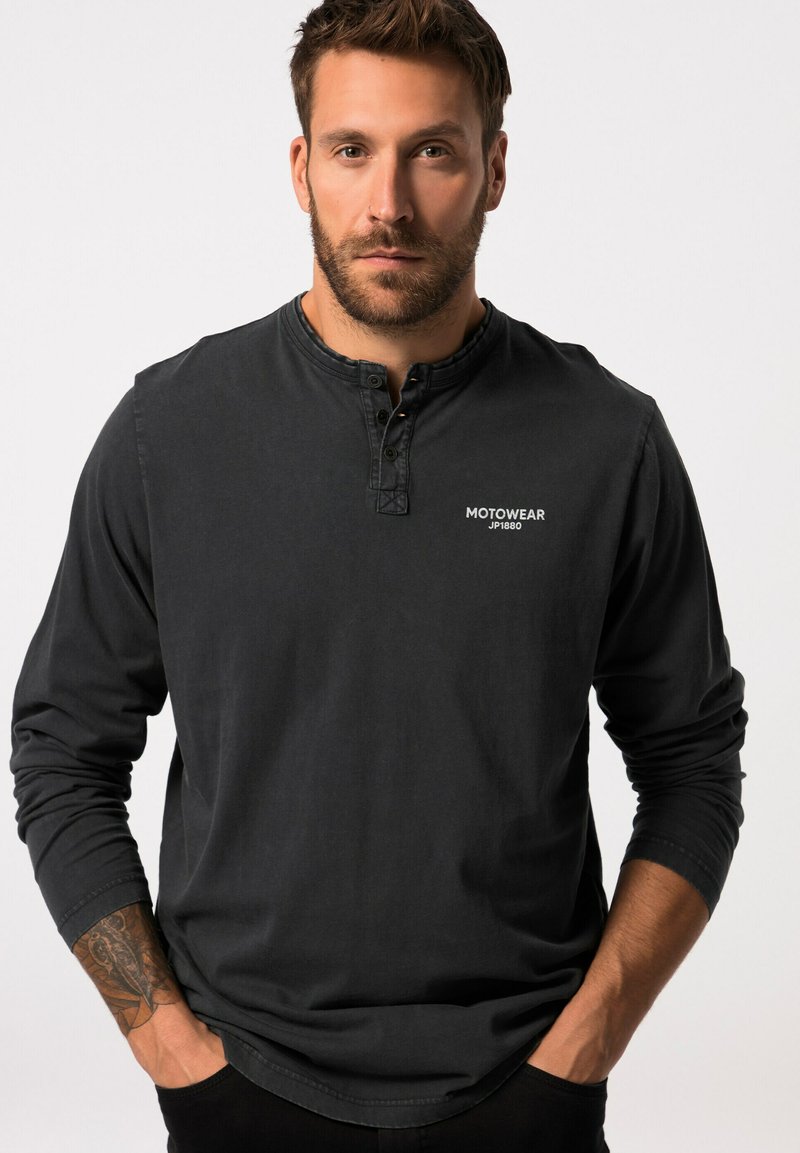 Langärmliges schwarzes Shirt aus Baumwolle mit einem geknöpften Henley-Ausschnitt und einem kleinen weißen Logo auf der Brust, mit lockerem Schnitt.