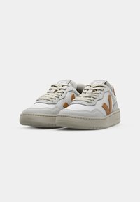 White textured sneakers with light brown accents, featuring a lace-up design, padded collar, and rubber sole.