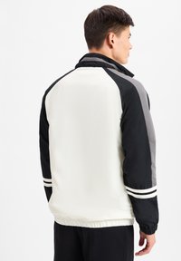 Chaqueta con una mezcla de paneles en negro, blanco y gris, diseño con cuello, puños elásticos y dos franjas blancas en cada manga.