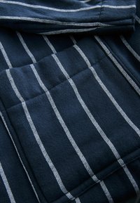 Jūras spēku audums ar horizontālām baltām svītrām, ar teksturētu apdari un vairākām kārtām, demonstrējot gludu, austu materiālu dizainu.