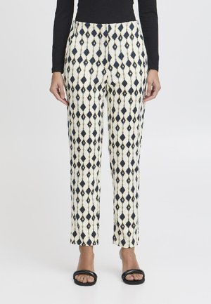 Patterned cropped pants in cream with navy diamond shapes and gold accents, made of lightweight fabric, paired with black sandals.