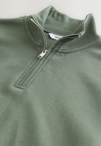Sweat-shirt vert olive doux à demi-fermeture éclair argentée avec un col plié sur un fond uni.